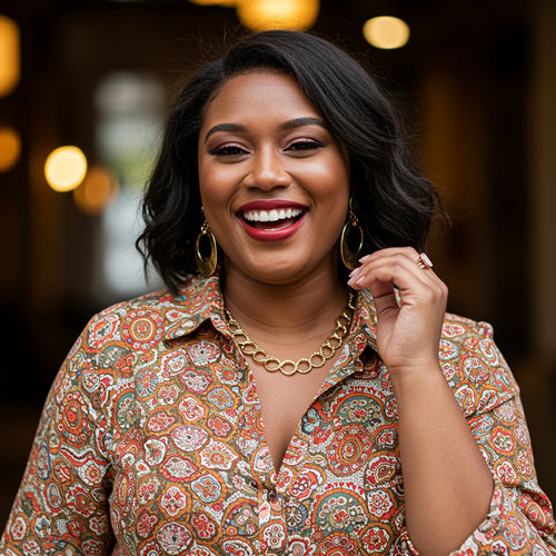 Woman wearing a patterned shirt with gold jewelry against a blurred background